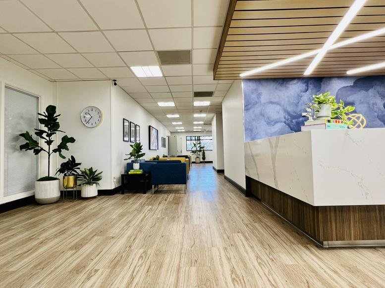 Spacious lobby at 9111 Cross Park Drive, Suite 200 with wood floors, plants, and a marble reception desk.