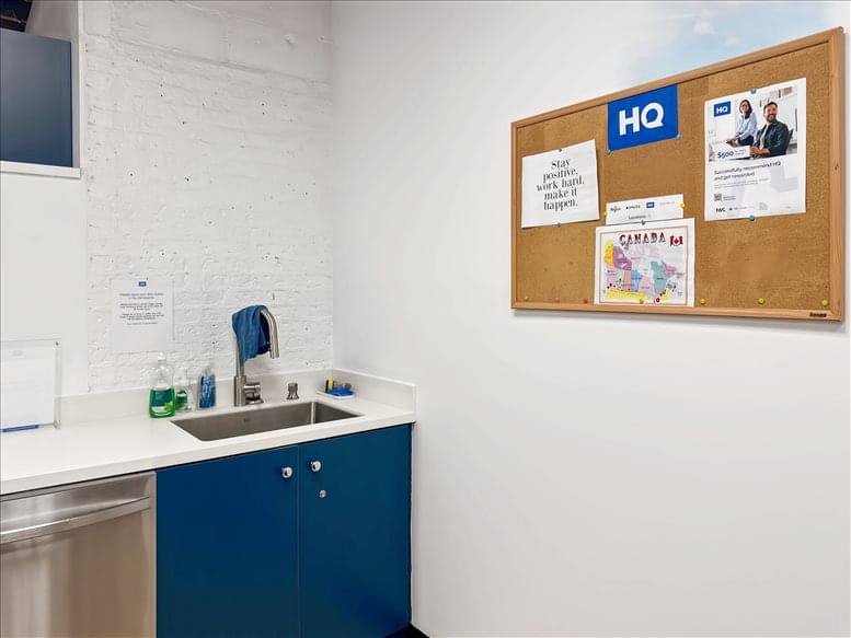 Breakroom kitchenette featuring a blue cabinet, stainless steel sink, and a cork notice board on the wall.