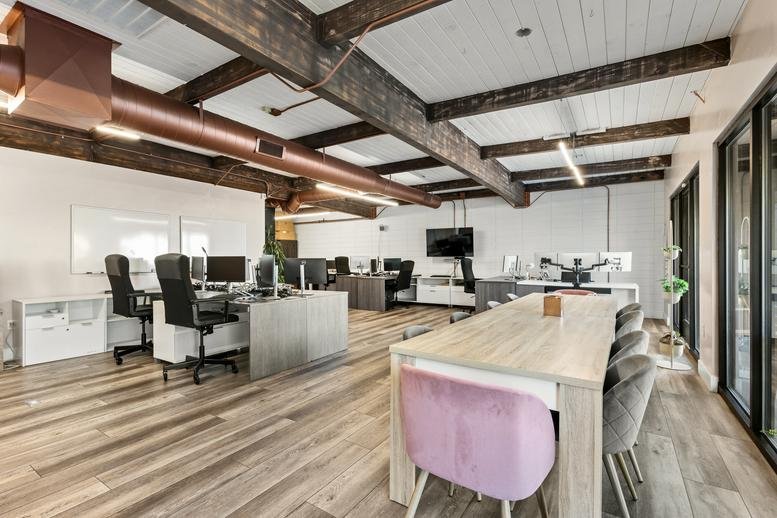 Open-plan workspace with wooden ceiling beams, copper piping, and a large communal table.