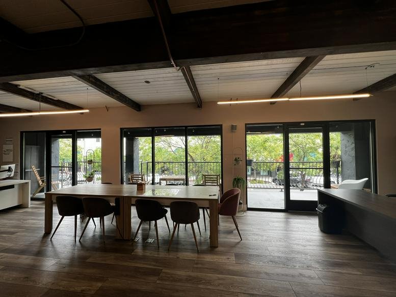 Spacious main hall with large windows, exposed wood beams, and a long wooden dining or work table.