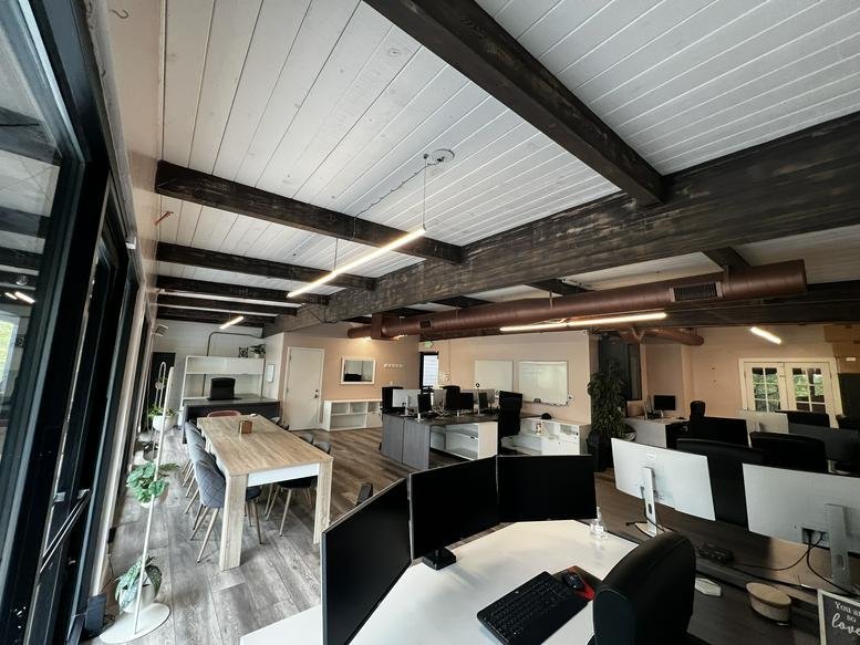 Spacious open-plan coworking area with exposed wood beams and multiple workstations.
