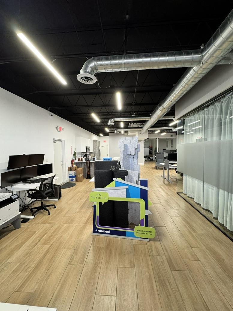 Bright open-plan office with wood-look flooring, exposed ductwork, and glass-walled meeting rooms.
