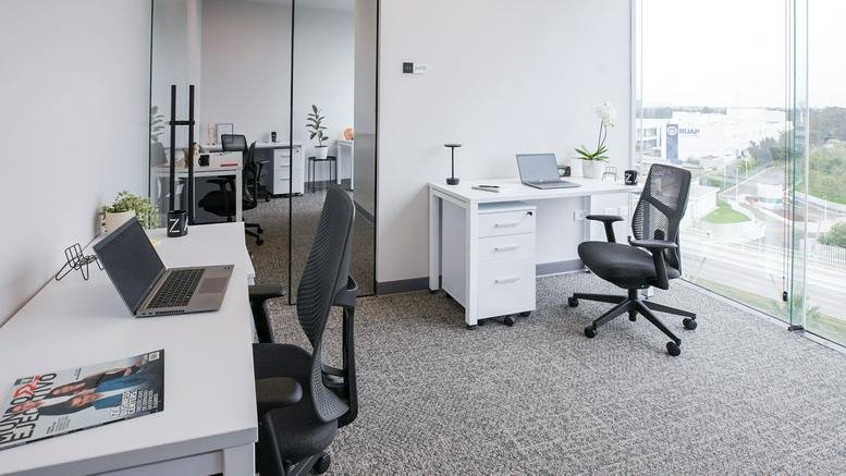 Private glass-walled office with two white desks and ergonomic chairs.