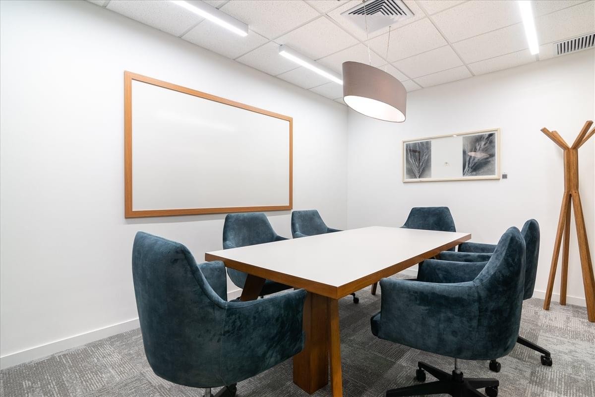 Spacious boardroom at Avenida Carrera 86 with blue velvet chairs and a wood-trimmed whiteboard.