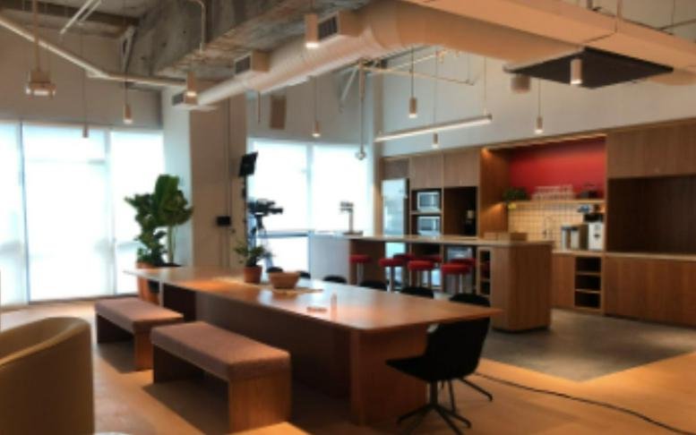 Large wooden communal table with bench seating in a bright, open-plan office area.