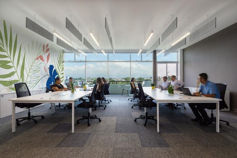 Spacious open-plan workspace at Avenida Escazú with tropical mural and panoramic mountain views.