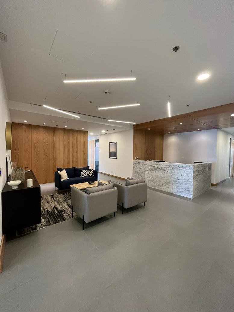 Spacious reception lobby with marble desk, grey armchairs, and warm wood wall panels.