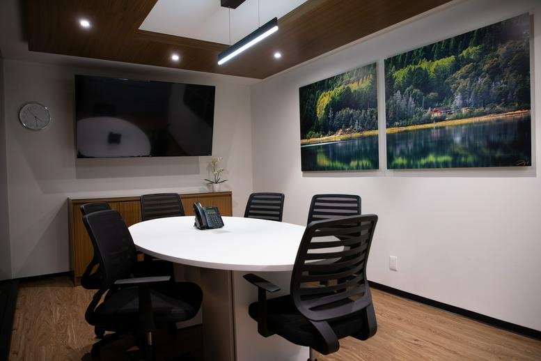 Small meeting room featuring a round white table, black ergonomic chairs, and nature-themed wall art.