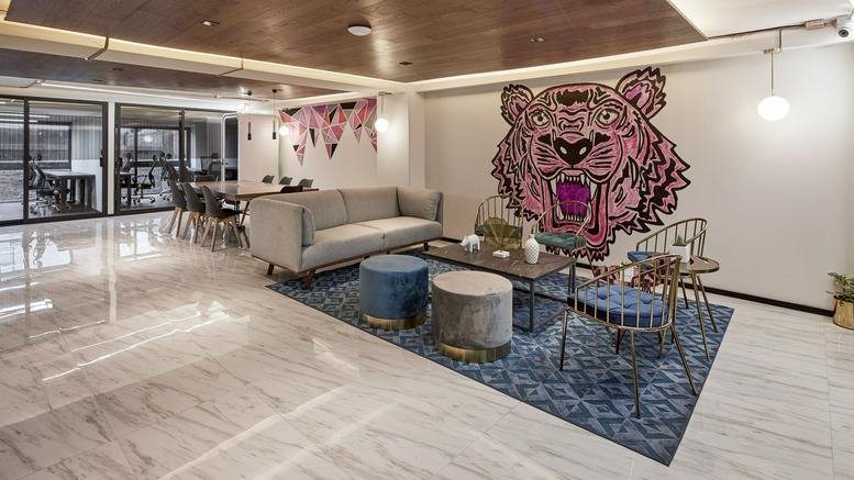 Modern lobby area featuring a large pink tiger wall mural, grey sofa, and blue velvet ottomans.