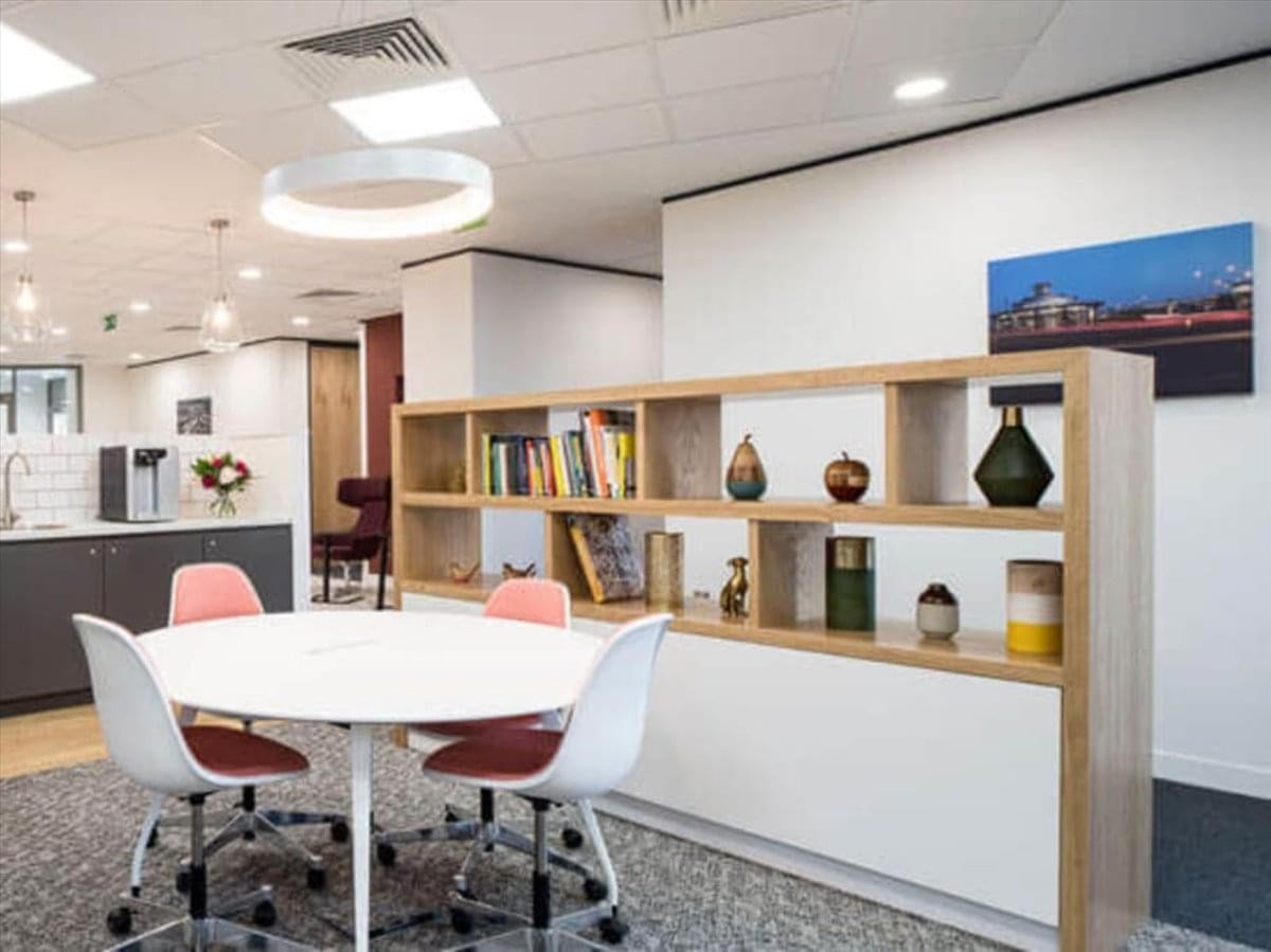 Coworking lounge at Carrera 10 No. 26-21 featuring a round table, pink chairs, and a wooden display bookshelf.