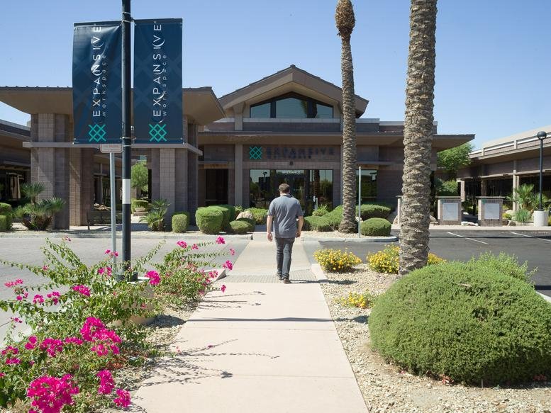 Walkway leading to the modern stone facade entrance of Cooper Crossing surrounded by desert landscaping.