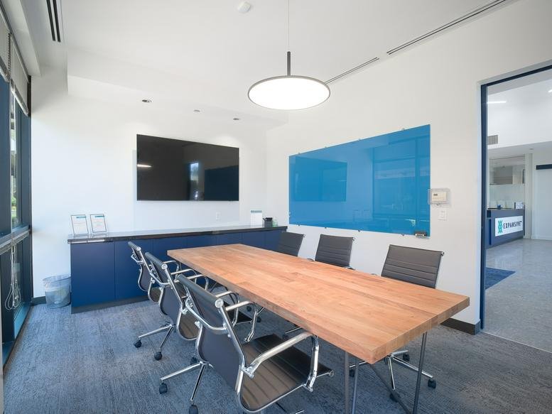 Contemporary meeting room with a live-edge wooden table and a blue glass whiteboard.