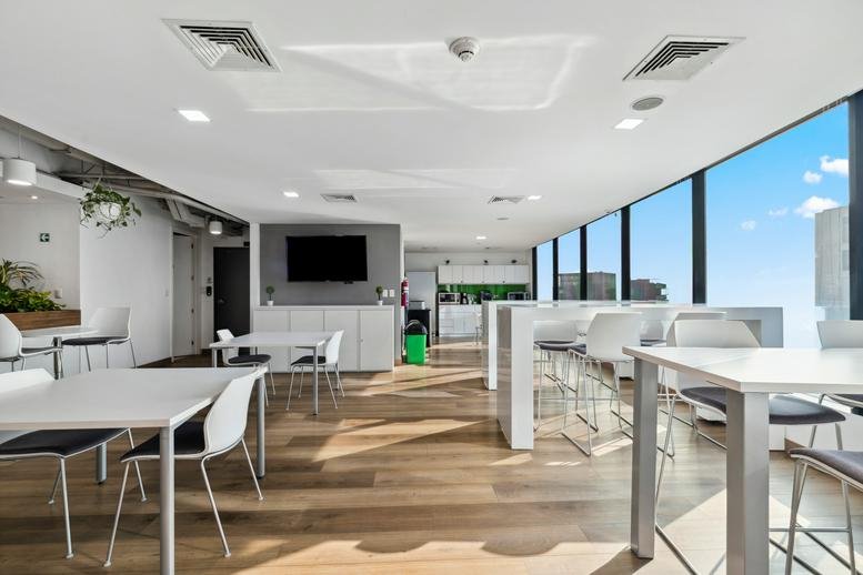 Open communal area with modern white tables, wooden flooring, and a flat-screen TV.