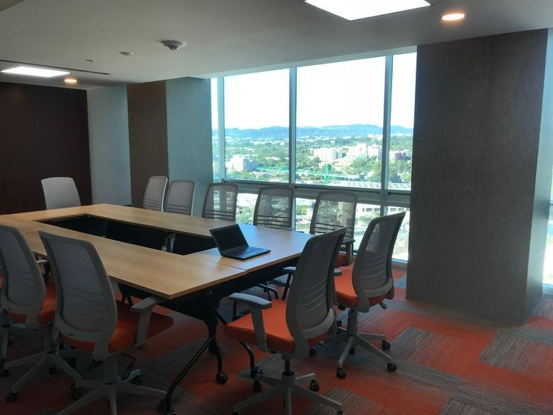 Large boardroom with a hollow wooden table, grey mesh chairs, and city views at Edificio Insigne.