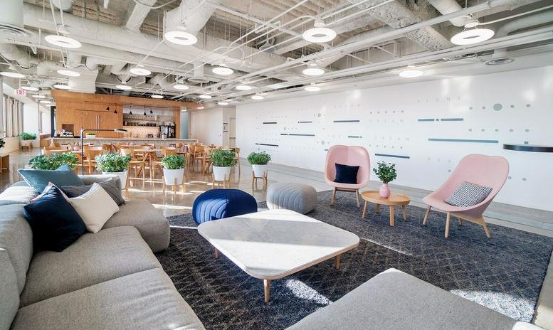 Modern breakout area with plush gray sofas, pink lounge chairs, and a large white wall.