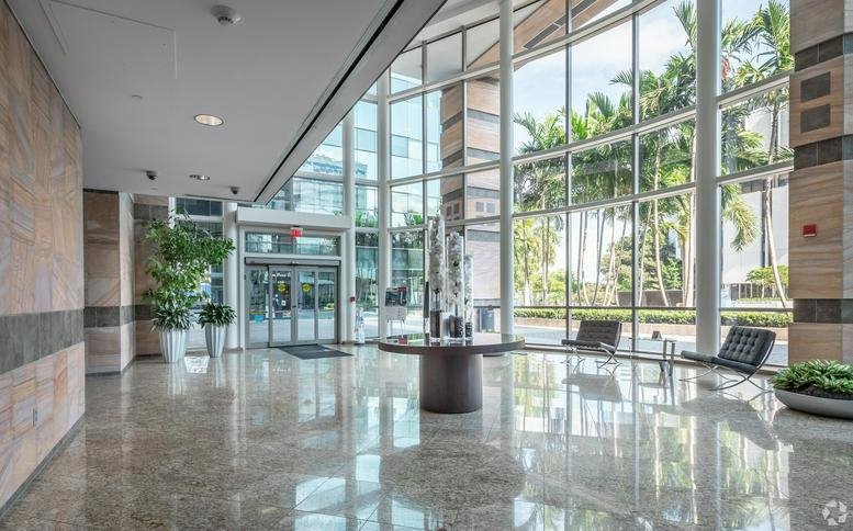 Large sunlit building lobby with floor-to-ceiling glass and polished stone floors.