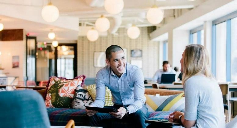 Spacious communal lounge at 1 Lincoln Street with colorful pillows, globe pendant lights, and people collaborating.