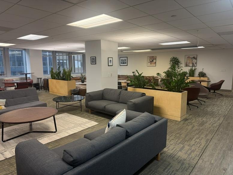 Modern lounge area at THE HUB, Church Street, New York City featuring grey sofas and wooden planters with greenery.