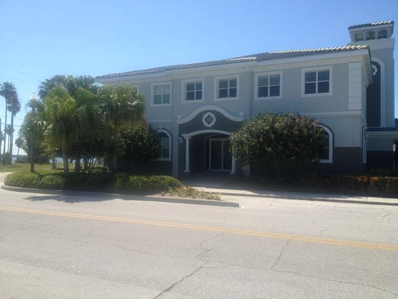 Exterior view of the two-story building for 100 Corey Executive Suites with palm trees and a blue sky.