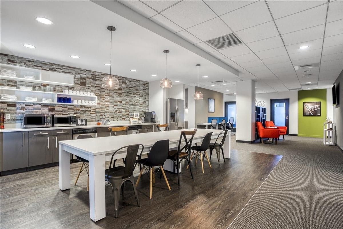 Spacious communal breakroom with a stone feature wall, kitchen, and long white dining table.