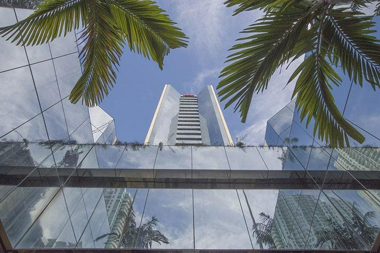 Looking up at the glass skyscraper of 1001 Brickell Bay through palm fronds and a reflective canopy.