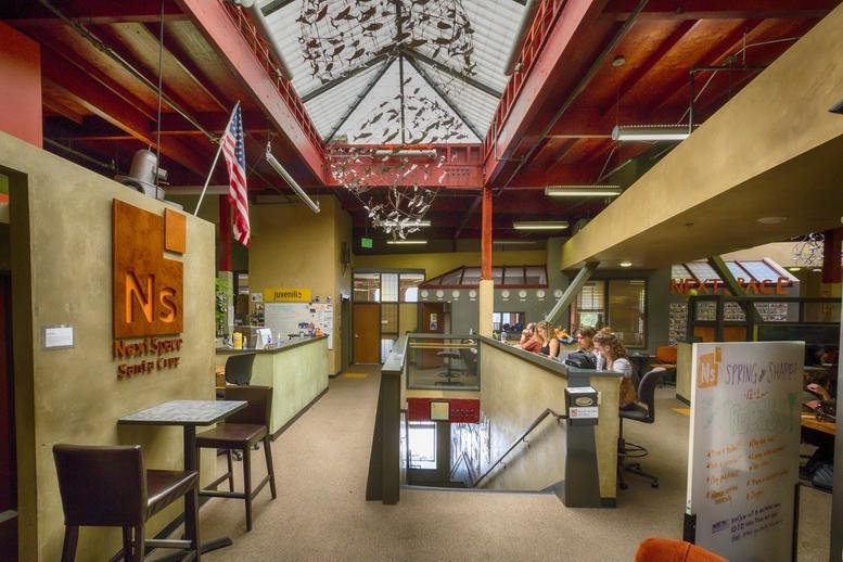 Spacious communal hub at 101 Cooper Street with high ceilings, exposed red beams, and a decorative skylight.