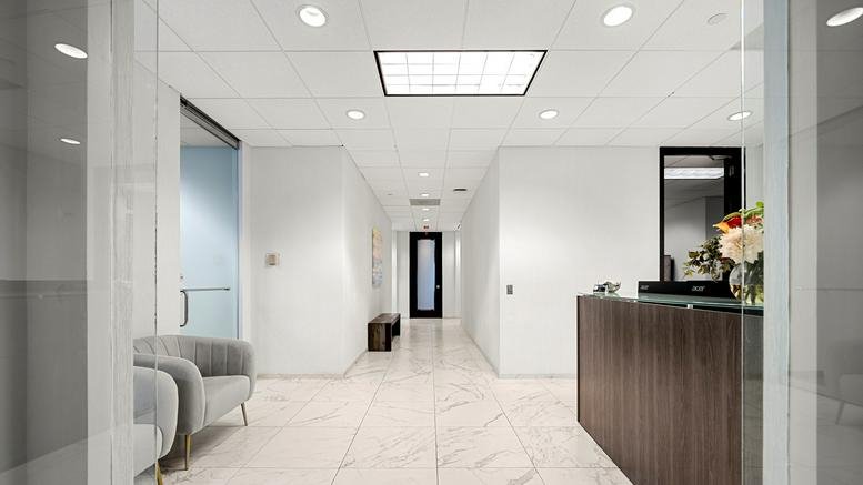 Modern lobby with white walls, marble flooring, and a dark wood reception desk.
