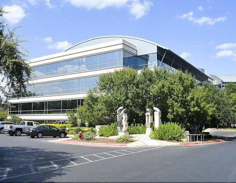 Modern multi-story office building with a curved glass facade and landscaped gardens.
