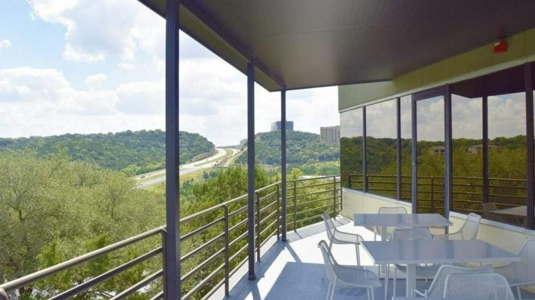 Balcony seating area with white tables and chairs overlooking a lush valley.