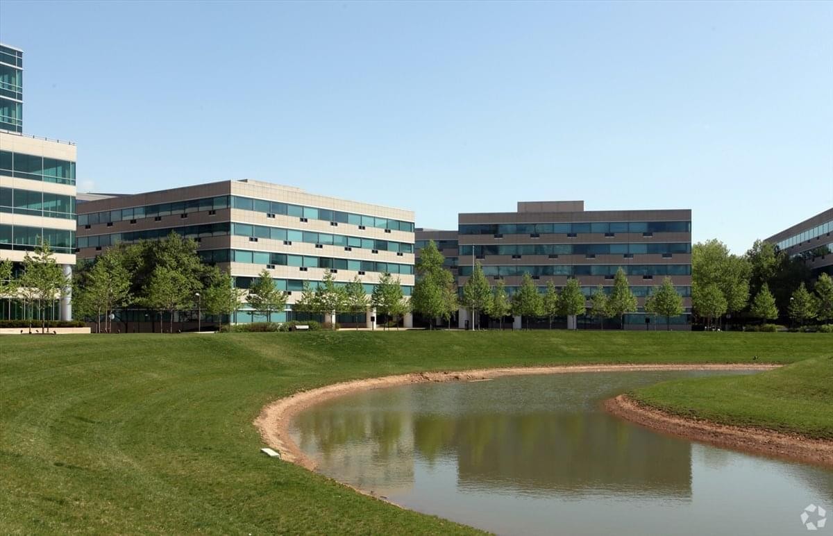 Landscaped office park exterior with a calm pond and several multi-story buildings.