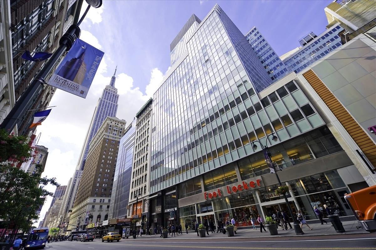 Exterior view of the modern glass facade at 112 W. 34th Street with the Empire State Building in the background.