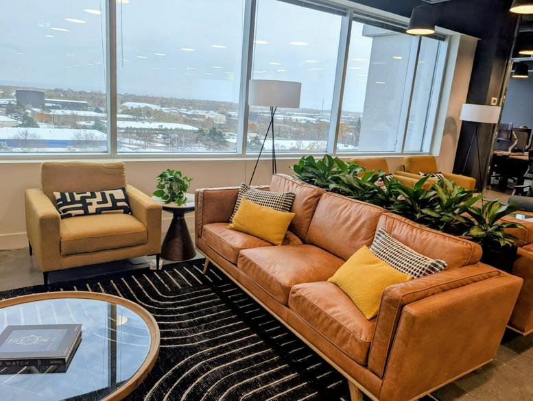 Bright communal lounge at Venture X Burlington, International Boulevard featuring tan leather sofas and large windows.