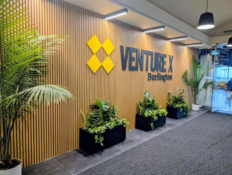 Branded reception wall at Venture X Burlington, International Boulevard featuring wood slats and greenery.