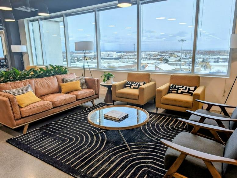 Sunlit common area at Venture X Burlington with leather seating, geometric rug, and panoramic views.