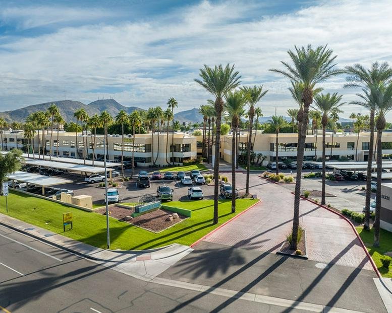 Wide aerial exterior view of the office park and parking lot surrounded by tall palm trees.