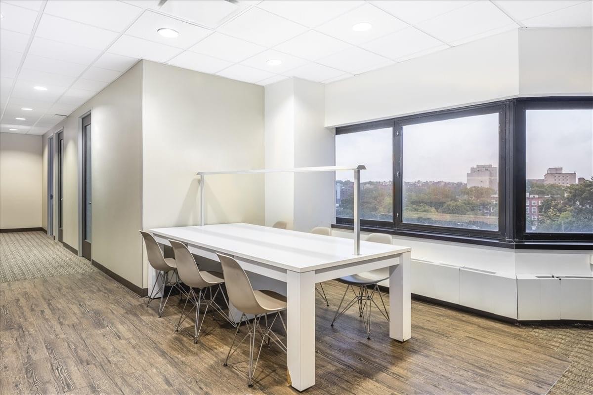Bright coworking area at 118-35 Queens Blvd. with a long white table and large windows.