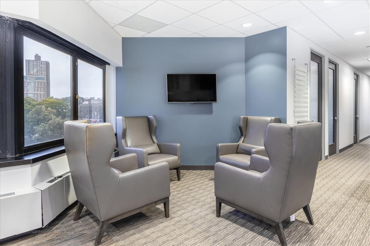Comfortable lounge area at 118-35 Queens Blvd. , Suite 400 with grey armchairs and a wall-mounted TV.