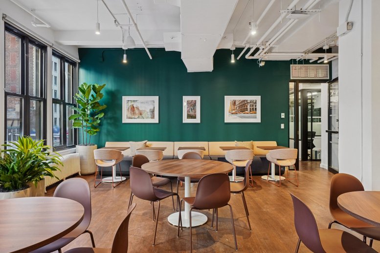 Spacious communal lounge at 120 East 23rd Street with a dark green accent wall and round wooden tables.