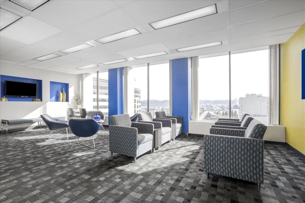 Spacious breakout lounge with grey armchairs, blue pillars, and city views through large windows.
