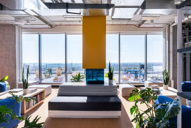 Bright modern lounge with a yellow feature pillar, blue seating, and indoor plants.