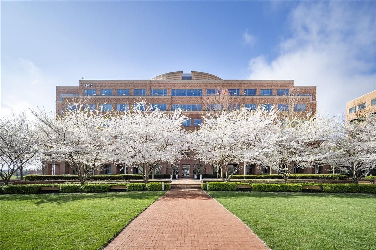 Exterior view of the brick building at 12410 Milestone Center Drive, Suite 600, framed by white cherry blossoms.