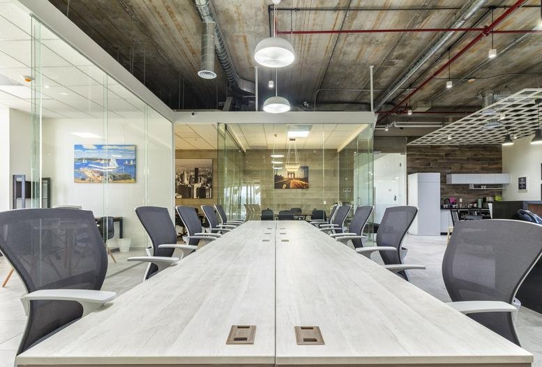 Long white meeting table with grey ergonomic chairs in a modern office with industrial ceilings.