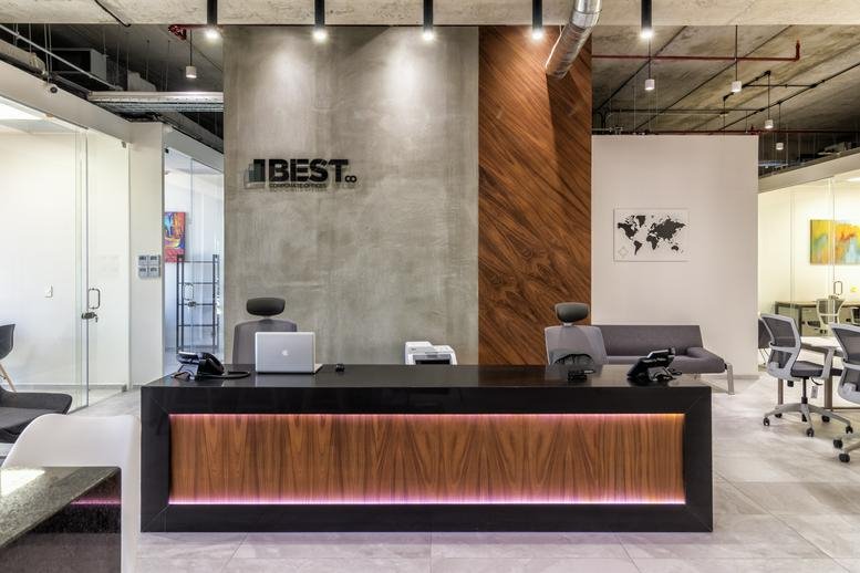 Modern reception desk with wood paneling and illuminated accents under industrial ceilings.
