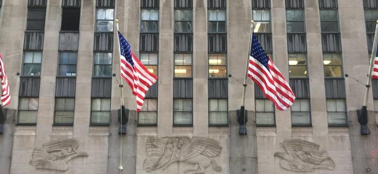 Exterior facade of the iconic limestone Rockefeller Center, 1270 6th Avenue, featuring American flags.