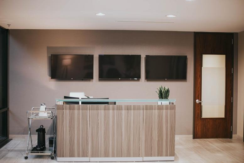 Minimalist reception desk with wood paneling and three wall-mounted screens.