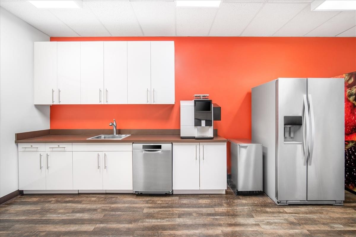 Modern communal kitchen at Central Park Corporate Center featuring orange walls and stainless steel appliances.