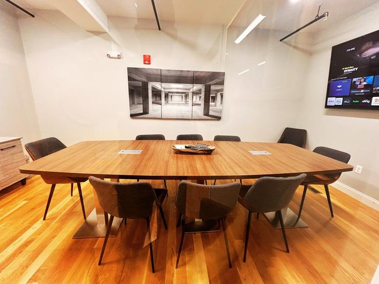 Large professional boardroom with a long wood table and wall-mounted TV at Burbspace.