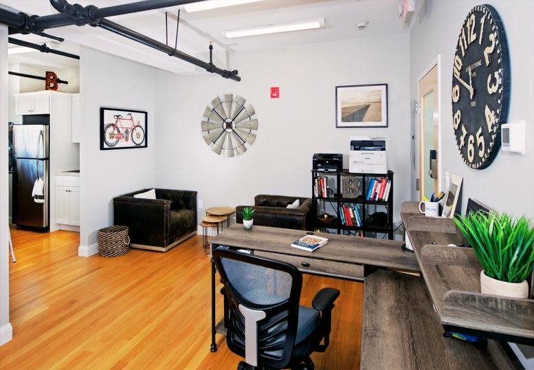 Open common area with lounge seating, workstations, and a large vintage-style wall clock.