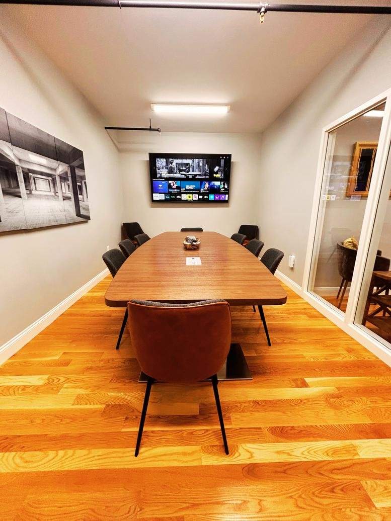 Conference room at Burbspace with a long wooden table, black chairs, and a wall-mounted monitor.