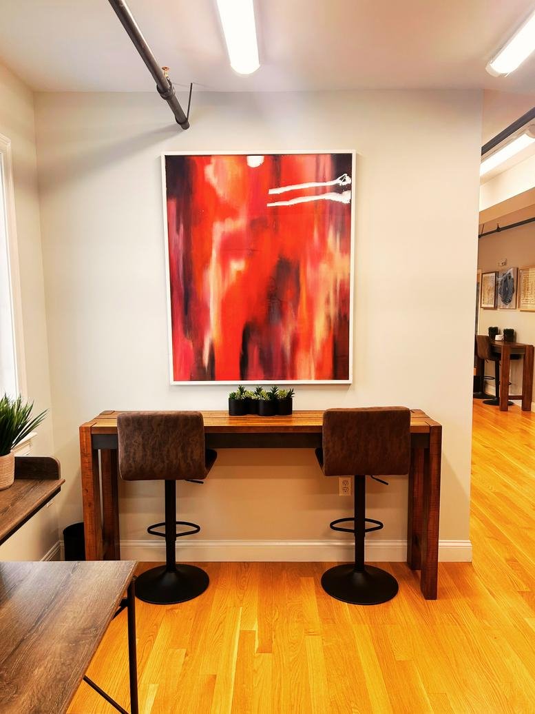 Communal seating nook featuring a tall wooden table, red abstract art, and bar stools.